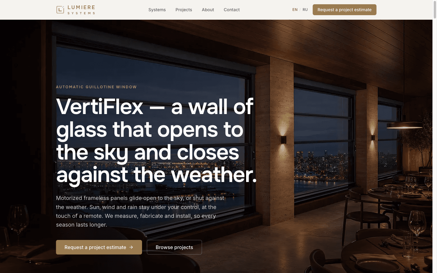 Lumiere Systems hero: a dark cinematic restaurant interior with VertiFlex glazing, a brass 'Automatic guillotine window' eyebrow, a large headline about a wall of glass that opens to the sky and closes against the weather, and a brass 'Request a project estimate' button.